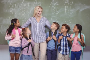 Happy teacher standing with schoolkids in classroom