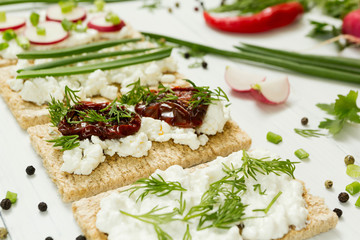 Sandwiches from goat cheese with sun dried tomatoes in olive oil with vegetables on a white wooden background.