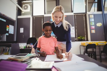 Obraz premium Teacher helping schoolgirl with her homework in classroom