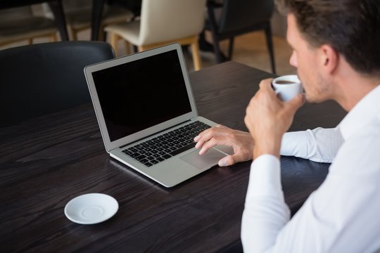 Businessman drinking coffee while using laptop in restaurant