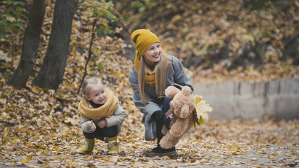 Little blonde girl with her mommy in autumn park - play and clap hands, close up