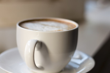 Cappuccino coffee in white cup on window