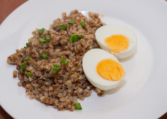 Buckwheat and two boiled eggs on a white plate. Wooden background