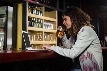 Man having beer while using laptop at counter