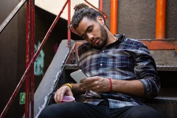 Man using mobile phone while having drink on staircase