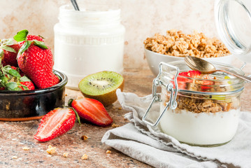 Healthy breakfast. Diet. Overnight oatmeal in a can, muesli. Yogurt with homemade granola and organic fruits - kiwi, banana, strawberry. On tray on stone table.  Copy space