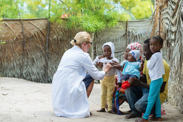 Caucasian female doctor listening heart beat and breathing of little African girl , family looking...