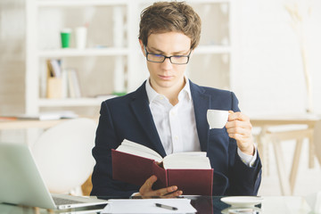 Attractive businessman drinking coffee and reading book