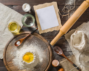 Ingredients for cooking dough or bread. Broken egg on top of a bunch of white rye flour. Dark wooden background.