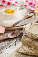 Ingredients for cooking dough or bread. Broken egg on top of a bunch of white rye flour. Dark wooden background.