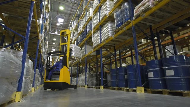 Warehouse worker on stacker loading cargo on rack