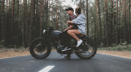 Obraz na płótnie Canvas Young Caucasian couple on a motorcycle on the forest road. Love, freedom, togetherness concept. Couple travel on a motorbike