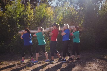 Group of fit women carrying a heavy wooden log 