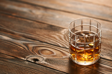 Glass of whiskey with ice cubes on wooden table
