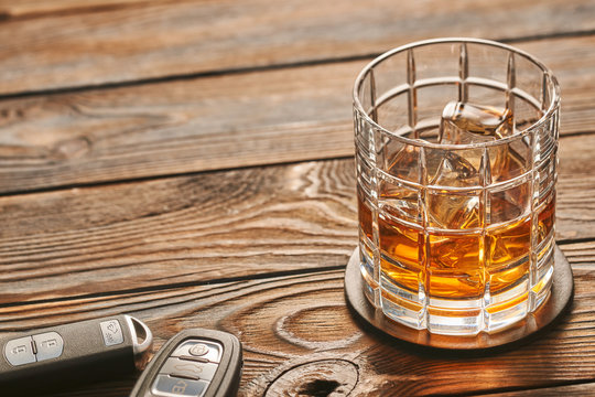 Glass of whiskey or alcohol drink with ice cubes and car key. Drink and drive concept.