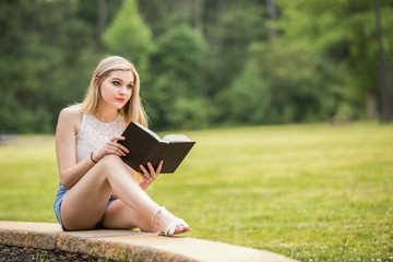 Obraz premium Teenage girl with a book in the park during the summer.