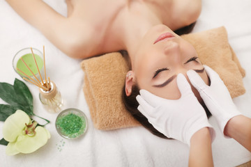 Beautiful young woman getting facial massage lying on the couch. Top view focused on the face