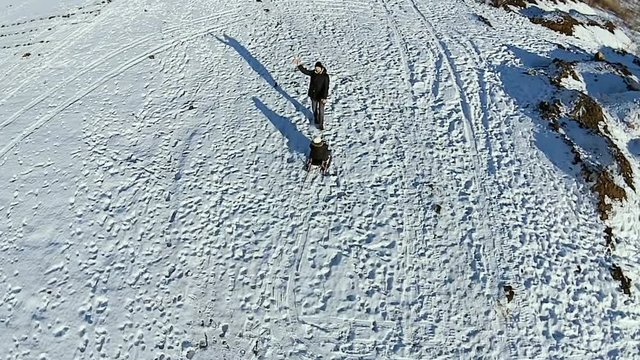 Aerial. Dad rolls his son on a sled. Dady and baby have fun. Man playing with boy and thumb up.