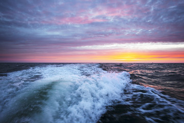 A wake of a motorboat at sunset time