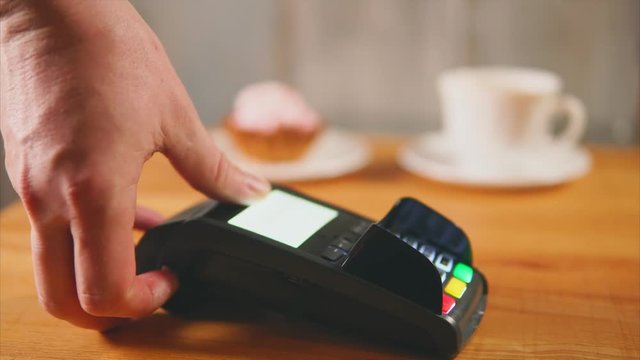 Close up view of contactless payment in store. Vendor put the payment terminal on the table and customer paying a bill by contactless method with his credit card.
