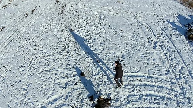 Aerial. Dad rolls his son aroud on a sled. Dady and baby have fun on snow. Man playing with boy outdor.