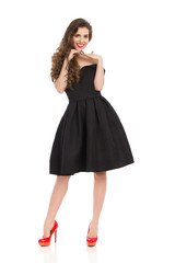 Charming Woman In Black Dress Is Posing With Hands On Chin