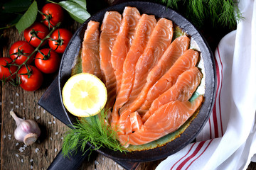 Homemade salted salmon with dill and cherry tomatoes on an old wooden background.