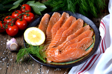 Homemade salted salmon with dill and cherry tomatoes on an old wooden background.
