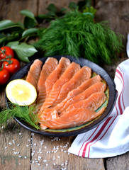 Homemade salted salmon with dill and cherry tomatoes on an old wooden background.