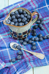 Blueberries in cup. Blue wooden table, blue kitchen towel.