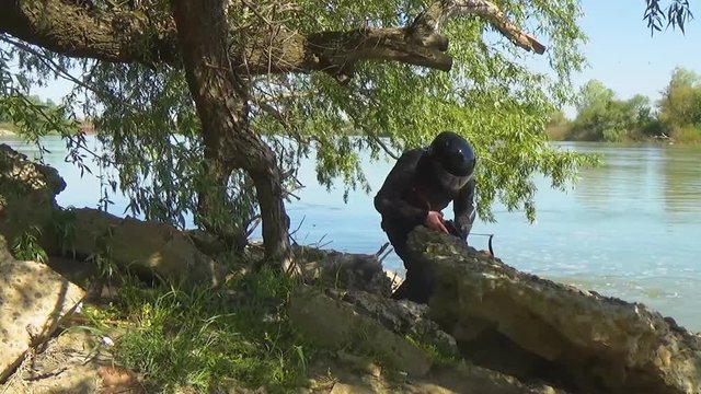 A Russian special forces soldier in armor and helmet goes to a position near the river bank and targets a crossbow. Marine recon.