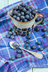 Blueberries in cup. Blue wooden table, blue kitchen towel.