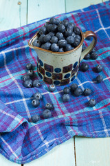 Blueberries in cup. Blue wooden table, blue kitchen towel.