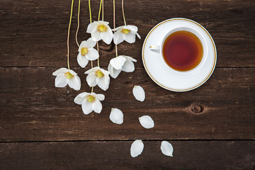 A cup with tea, white flowers of anemones on a wooden background. View from above.