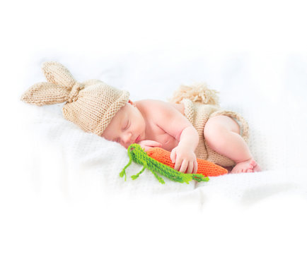 Cute two weeks old smiling newborn baby boy wearing knitted bunny costume, hat with rabbit ears, tail and funny carrot toy. Sweet baby portrait
