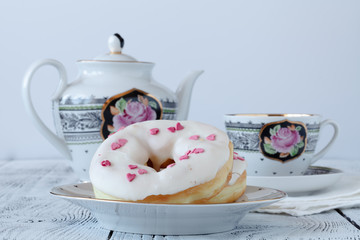 Donuts with white icing and sprinkling on wooden board with cup of coffee