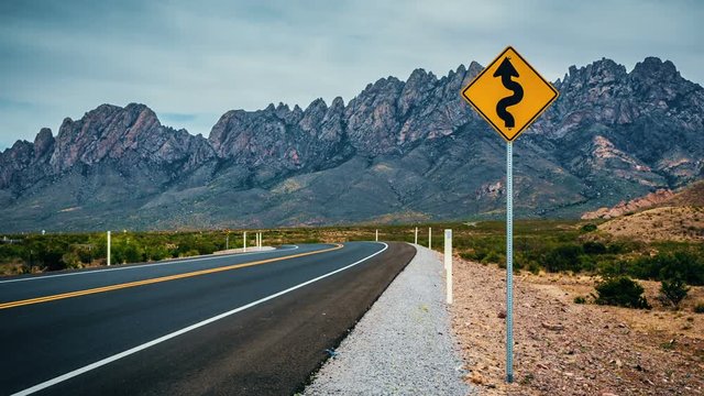 Twisty Road Sign Panning Mountain Road Time-lapse. a panning right time-lapse of a twisty road sign on the roadside with mountain range in the background

