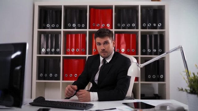 4k uhd. Young attractive successful businessman showing you fuck sign third finger inside office with table, computer, digital pad, lamp. middle shot teal and orange