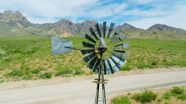 Aerial Flying Over Old Spinning Windmill. a drone view flying over an old windmill spinning with a desert and large mountain range in the background. Slow motion
