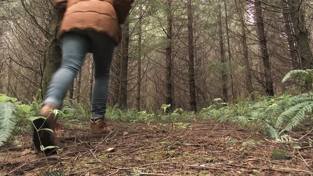 Low angle shot of woman walking on forest trail into dense forest in Washington State.