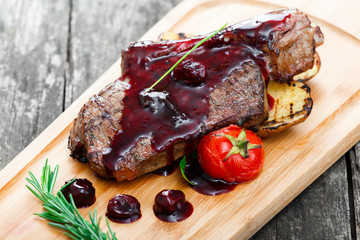 Roasted Pork steak on bone stuffed with cheese, grilled vegetables and berries on stone slate background on wooden background close up. Hot Meat Dishes. Top view with copy space