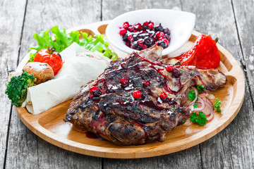 Roasted Pork steak on bone stuffed with cheese, grilled vegetables and berries on stone slate background on wooden background close up. Hot Meat Dishes. Top view with copy space