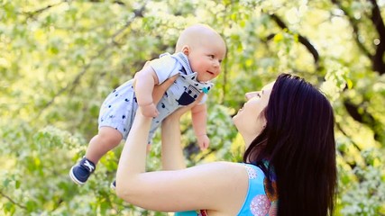 Young Mother Holding Her baby son aloft in park or garden