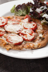  
Homemade pizza with marinara sauce topped with parmesan cheese and sliced tomatoes with a side salad up close shot
