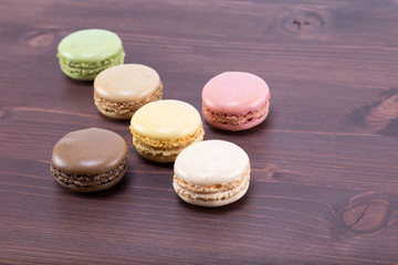Six tasty and colorful macaroons on a natural ipe wood dark brown table - form of an arrow