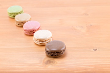 Five tasty and colorful macaroons in line on a natural oak wood brown table