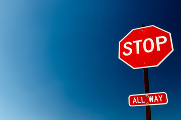 All way stop sign against bright blue sky.