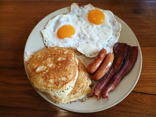 American Breakfast double fried egg,Bacon and sausages serve with butter pancake on white plate on wooden table, Homemade Continental breakfast at home kitchen, Hotel breakfast
