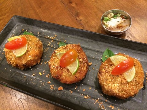 Fish cakes and bread crumbs decorate with tomato,lime and basil leaves, Delicious homemade Haddock fishcakes with Thai spicy dip on black plate in restaurant, selective focused with blur background