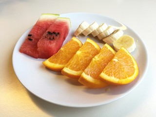 Healthy fresh mix fruits, Plate of Orange slice, banana slice and 2 pieces of watermelon isolated on white plate, foreground focused blur background